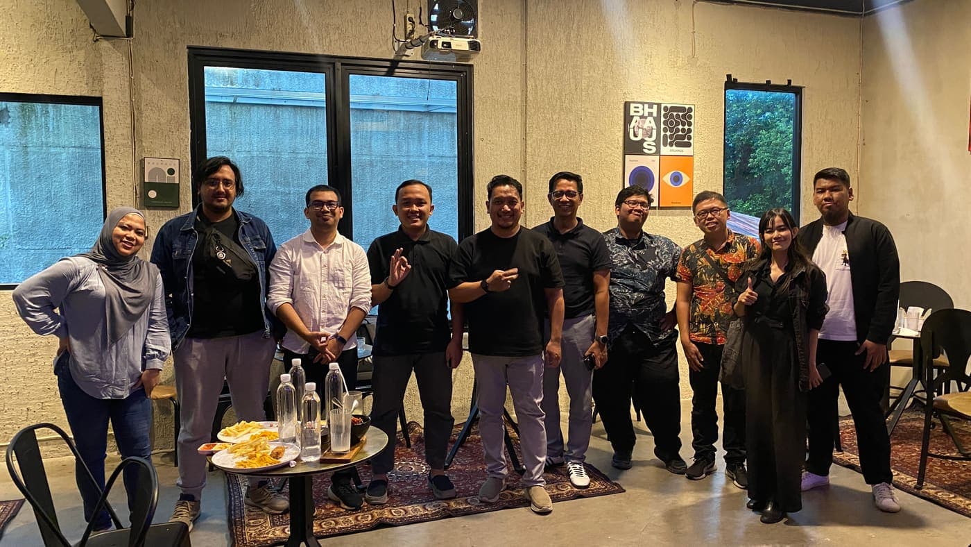Peserta meetup Tech Voice Indonesia berfoto bersama di ruang kafe dengan layar presentasi di belakangnya.